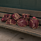 Maroon baseball gloves with gold stitching on a wooden bench against a green wall.